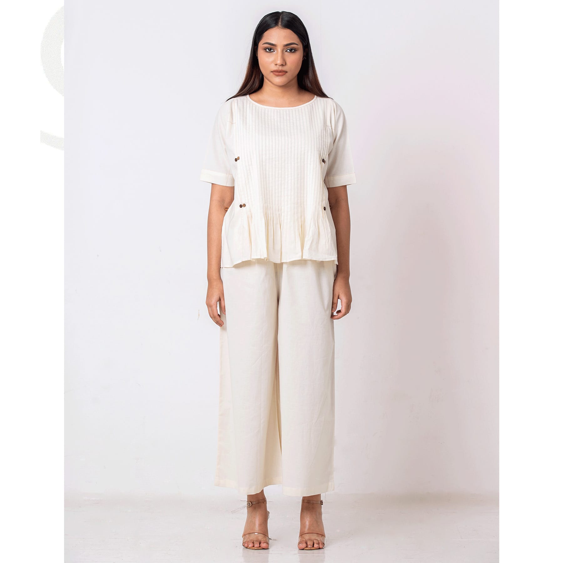 3A-Taan-Bangladesh-(Fahim-Fayshal-+-Tanha-Yesmin)-Sistainable-Fashion-brand,-Clothing-brand,-taanbd A woman wearing an ivory handmade co-ord set featuring a pleated peplum-style top with side-button details and wide-leg trousers. The outfit exudes minimalist elegance and sustainable fashion.